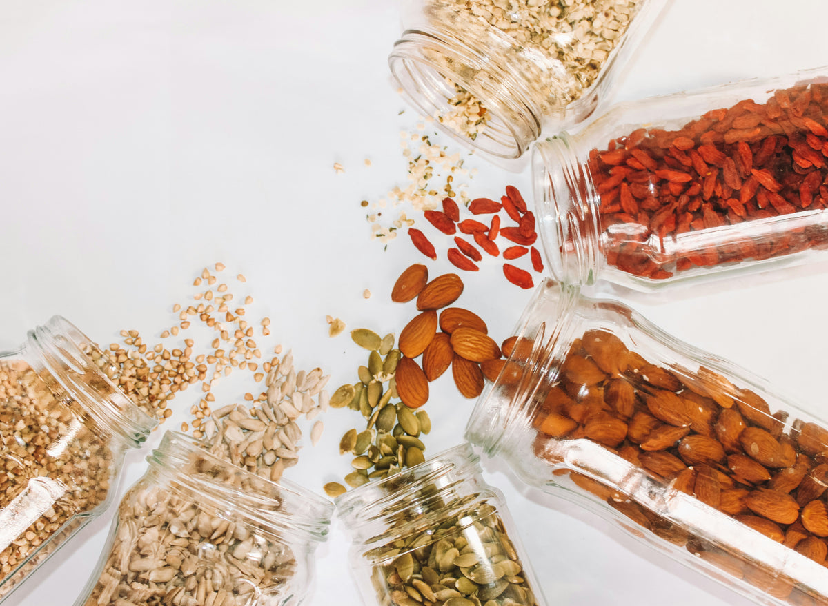 Glass jars filled with various seeds and nuts on a white background