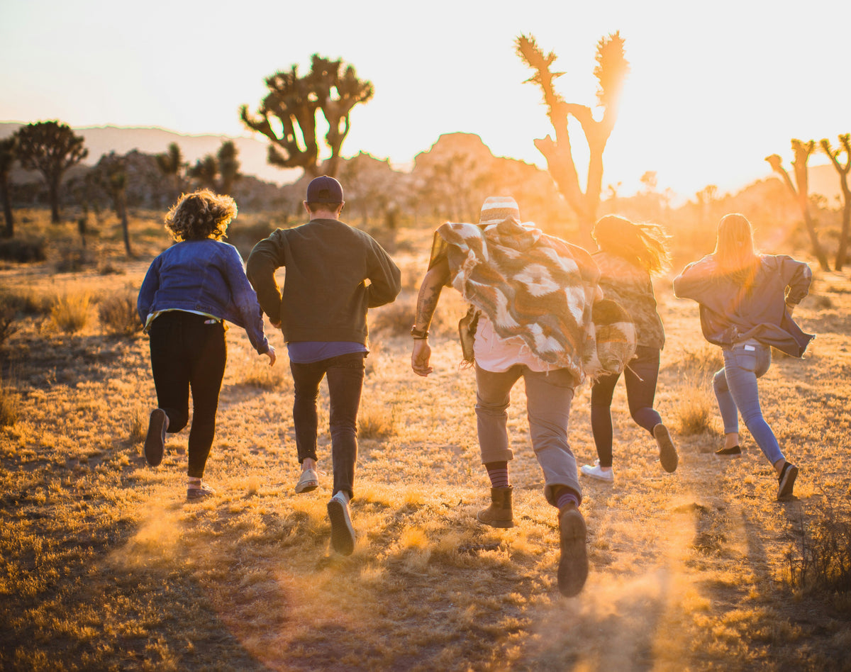 Group of people running through a desert landscape with cacti at sunset.