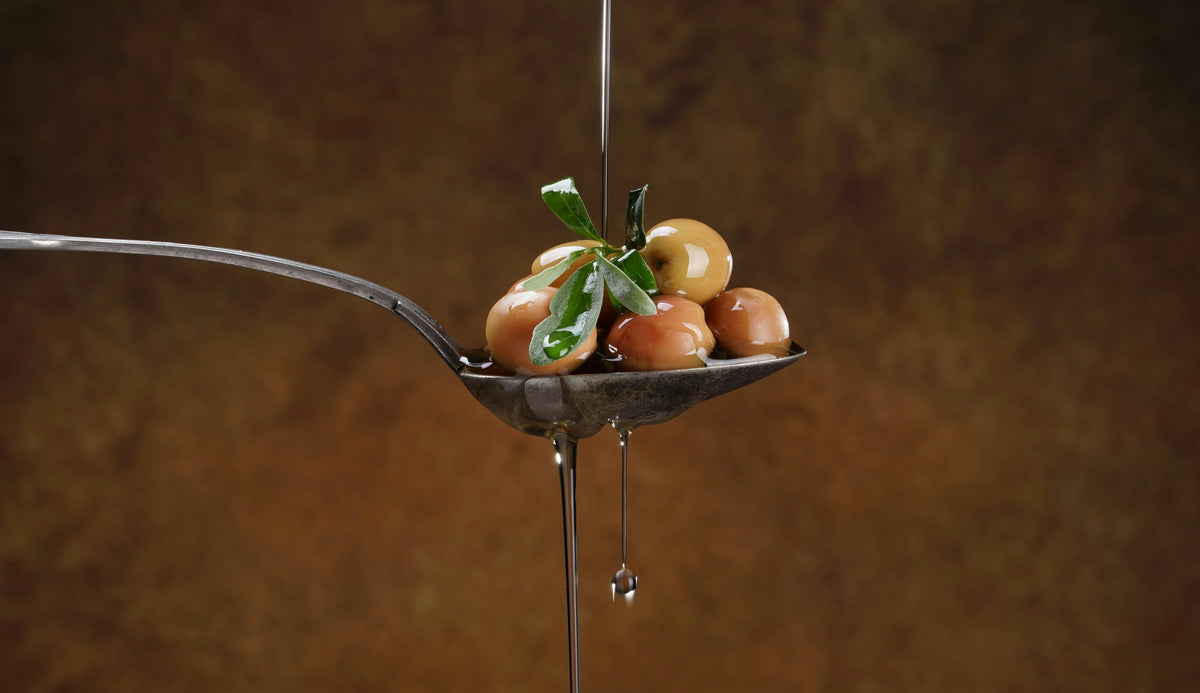 Spoon with olives and olive oil droplet against a brown background
