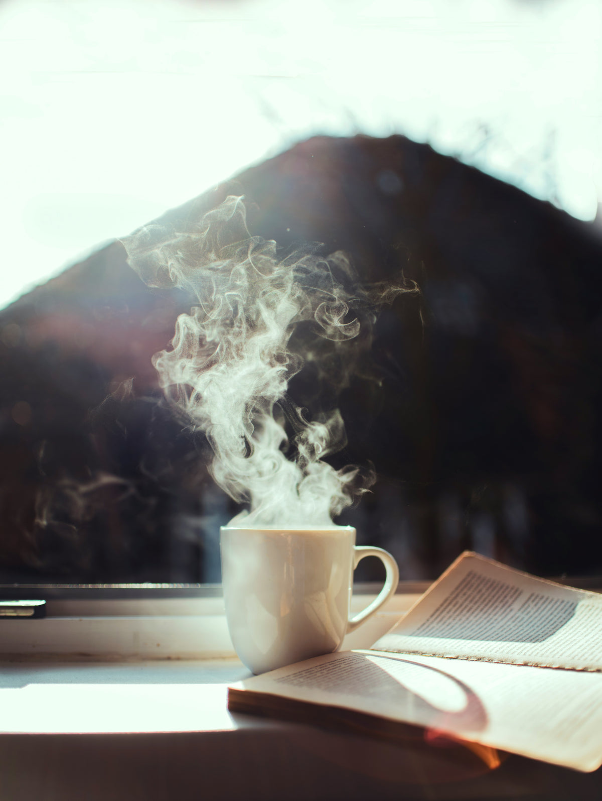 Steaming cup of coffee on a windowsill next to an open book
